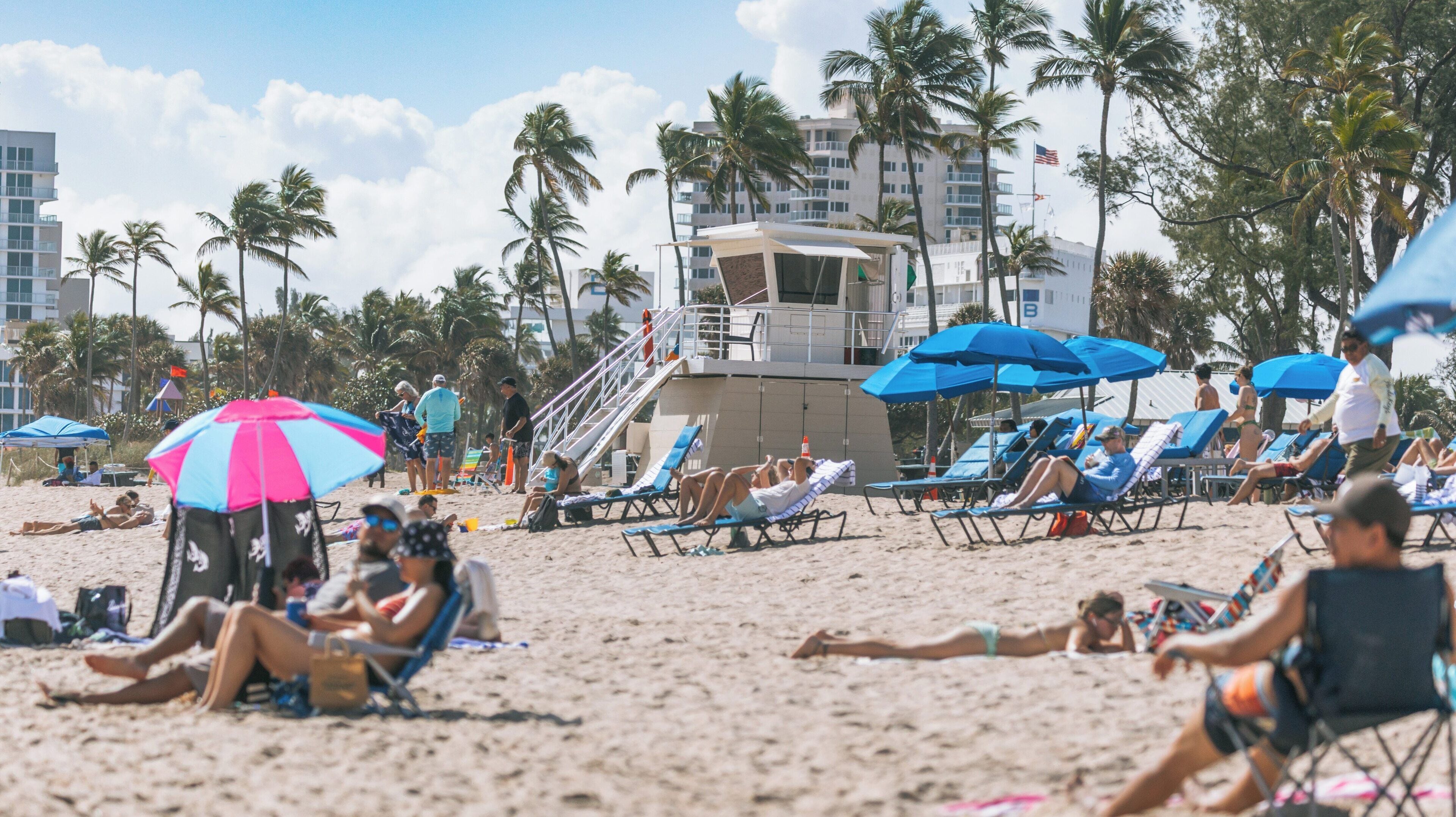 Enjoying a sunny day at Fort Lauderdale Beach with umbrellas and lounge chairs lining the sandy shore in East Fort Lauderdale, Florida during summertime fun