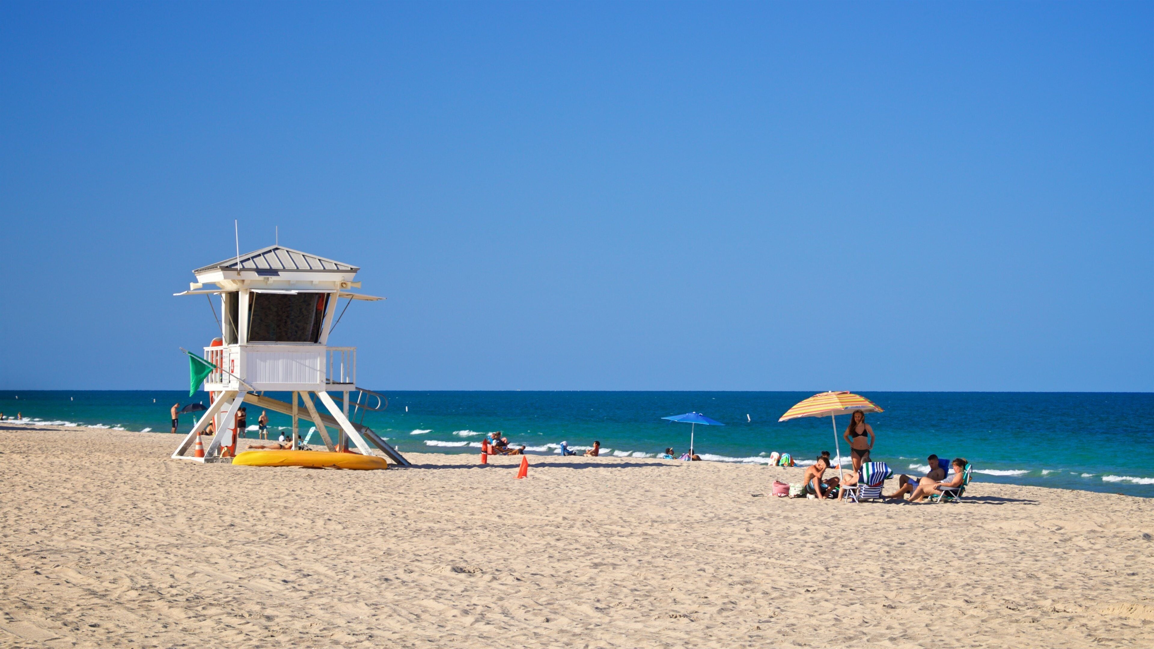 A lifeguard tower, beach umbrellas, and people relaxing on the sand.
