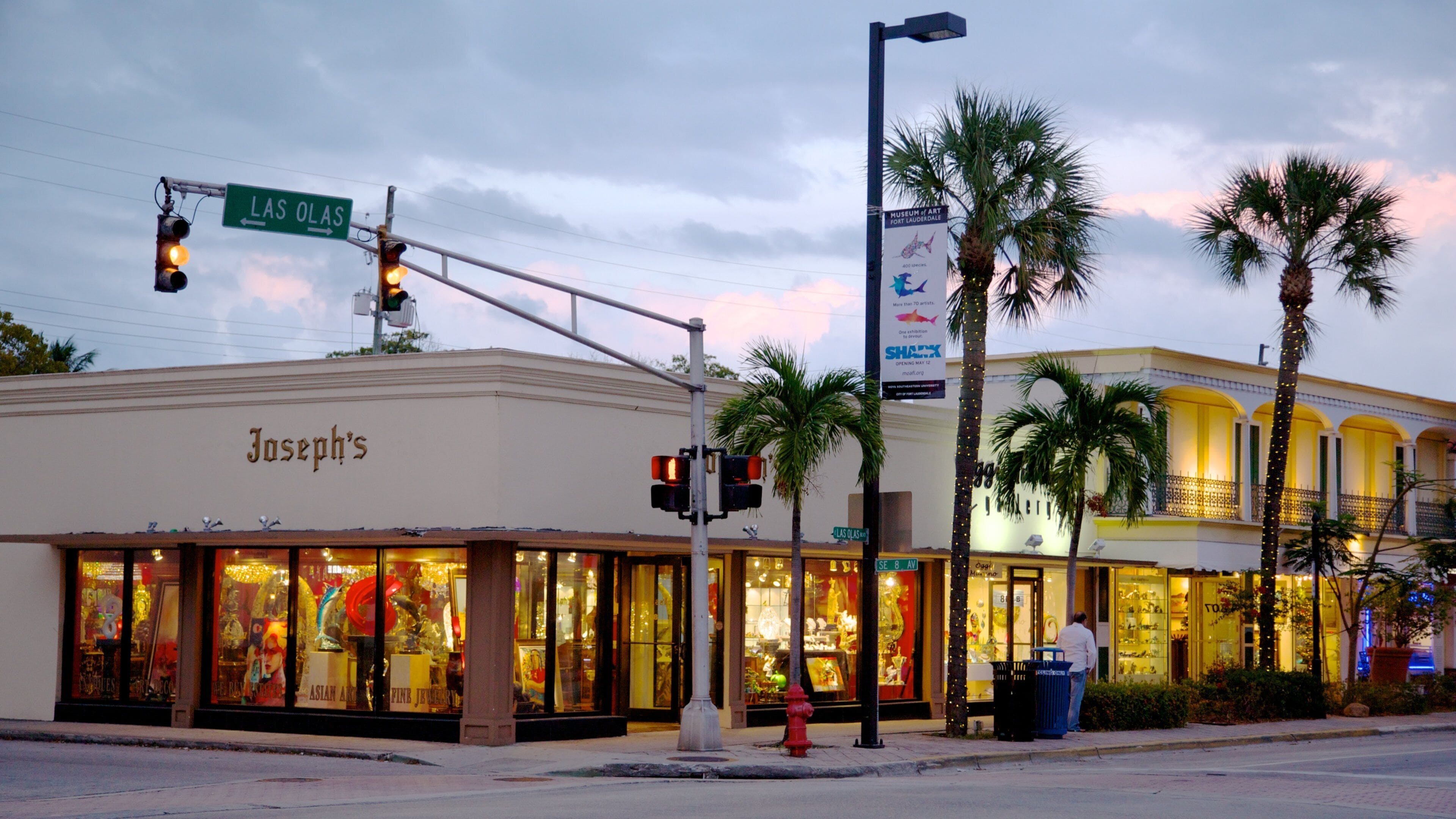 Una esquina de calle con una joyería llamada Joseph's, una palmera y un edificio con un cartel para el Museo de Arte.