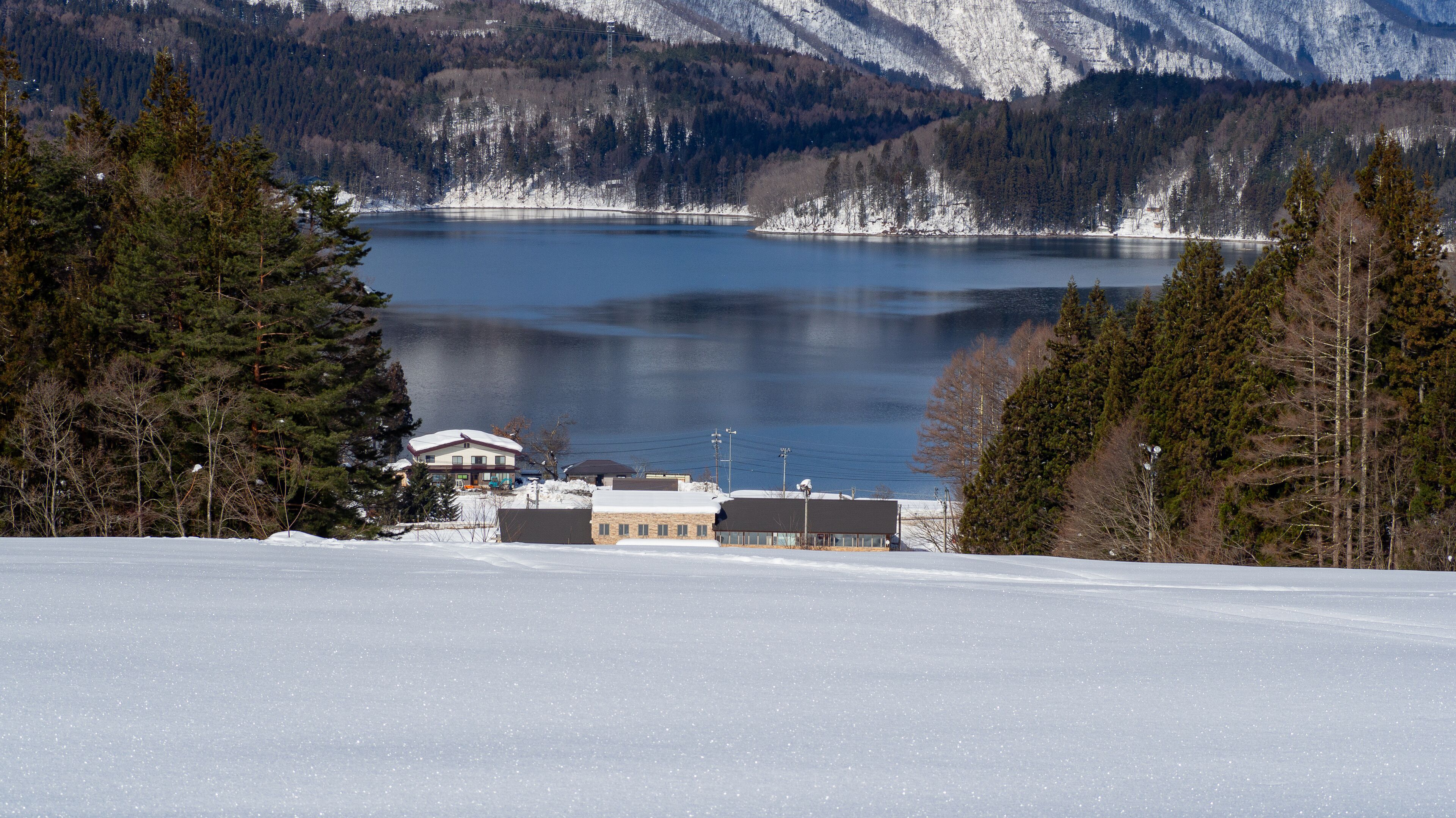 A snow-covered landscape with a lake, mountains, and a building in the foreground.