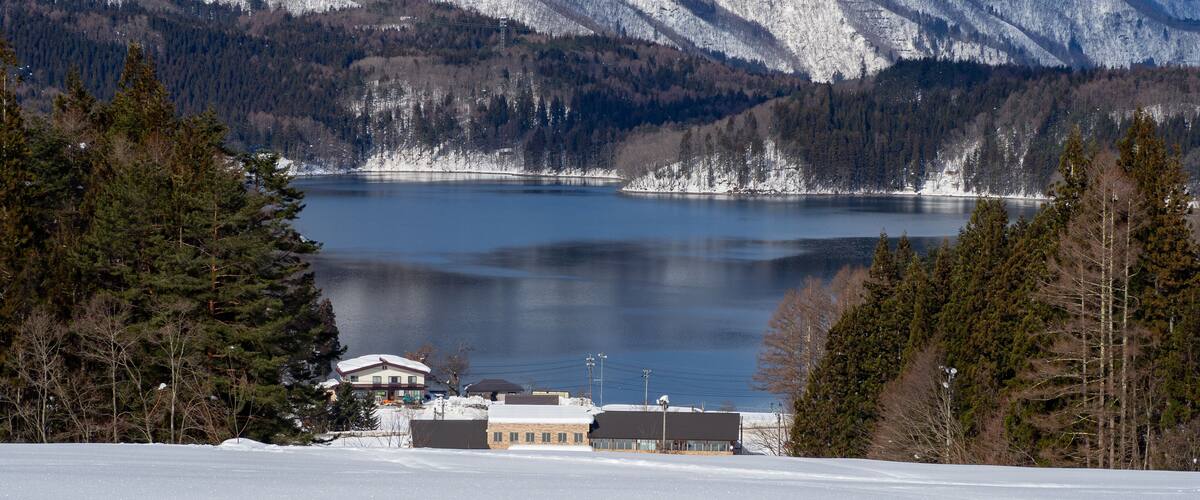 A snow-covered landscape with a lake, mountains, and a building in the foreground.