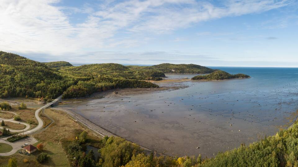 A coastal landscape with a beach, forested hills, and a road network.