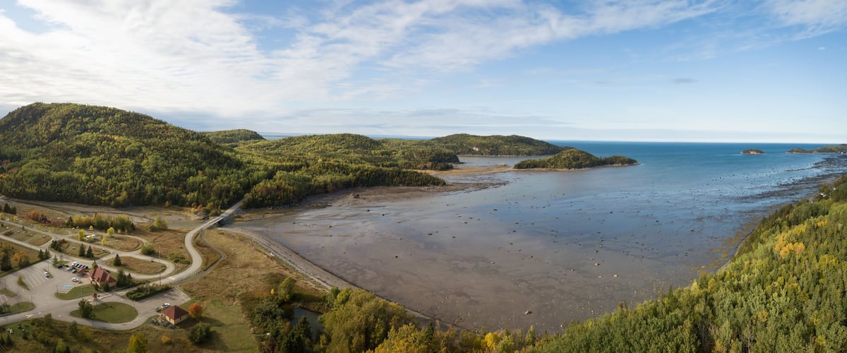 A coastal landscape with a beach, forested hills, and a road network.