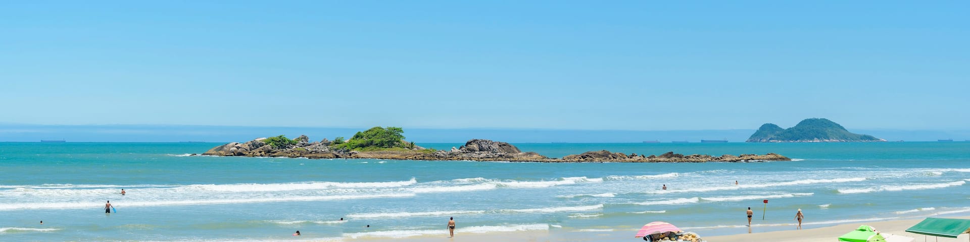 Panoramic view of a beach with two nearby islands. Sunbathers at Praia das Pitangueiras beach, Guaruja SP Brazil. Ilha Pompeba island in the middle and the Ilha da Moela island on the background.