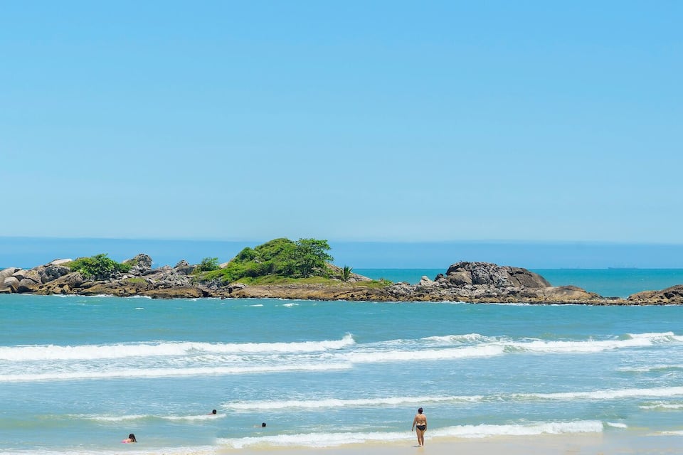 Una playa con agua azul cristalina, afloramientos rocosos e islas a lo lejos.