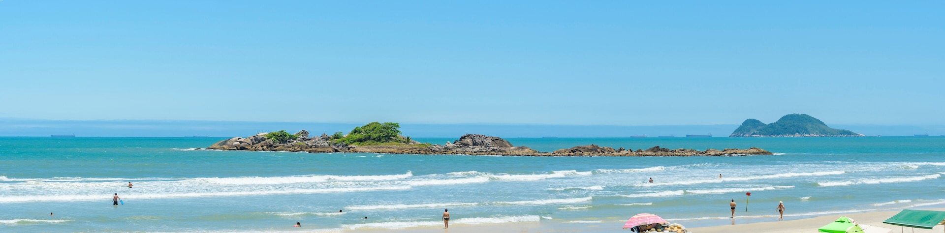Panoramic view of a beach with two nearby islands. Sunbathers at Praia das Pitangueiras beach, Guaruja SP Brazil. Ilha Pompeba island in the middle and the Ilha da Moela island on the background.