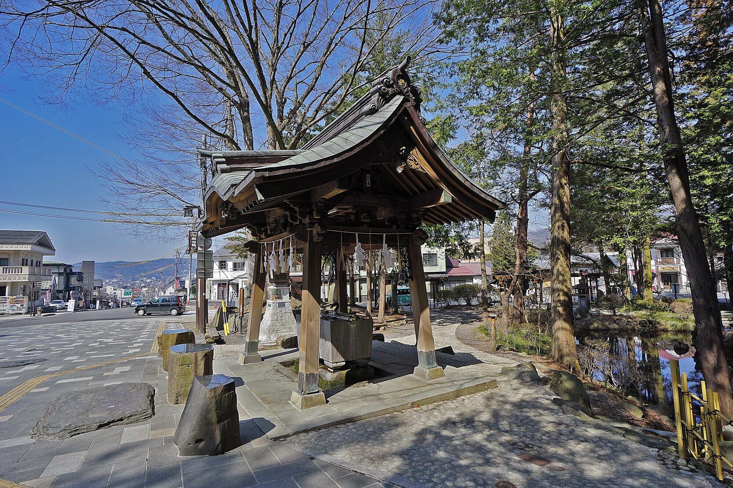 A traditional Japanese pavilion with a curved roof, surrounded by stone lanterns and trees.