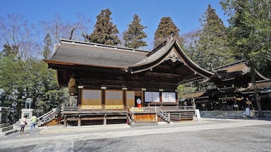 A traditional Japanese temple with wooden architecture, a stone statue, and a clear blue sky.