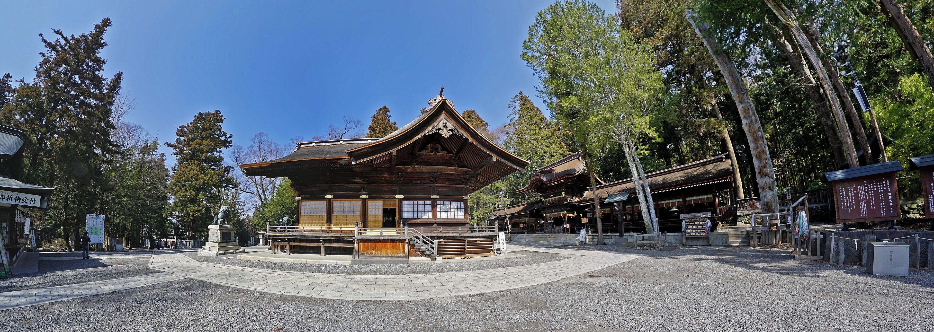 A traditional Japanese temple with a wooden structure, surrounded by trees and a gravel courtyard.