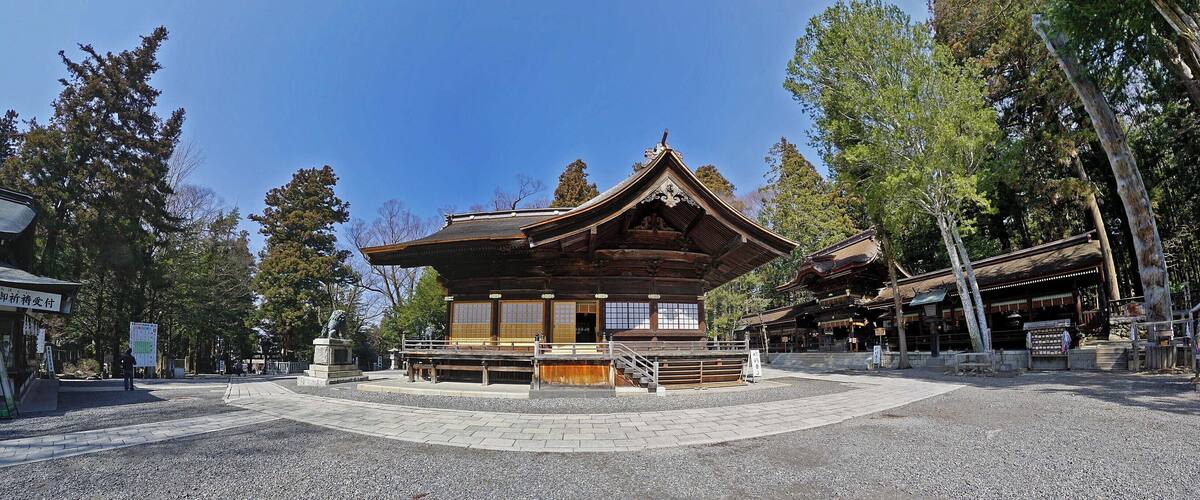 A traditional Japanese temple with a wooden structure, surrounded by trees and a gravel courtyard.