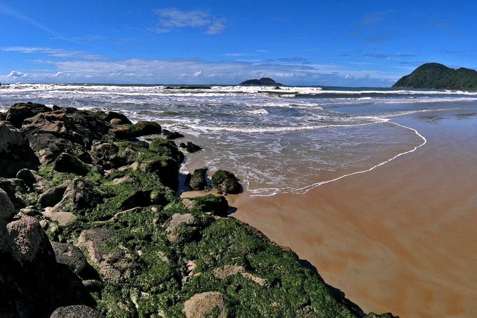 Una costa rocosa con olas rompiendo en la playa, rodeada de colinas verdes.
