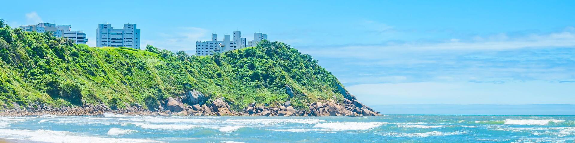 Beautiful Brazilian beach of the Paulista coast on a sunny day. The sea, some waves, the sand and a hill with some buildings on top. Photo at Praia do Tombo beach - Guaruja SP Brazil.