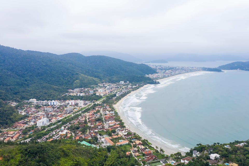 Uma cidade costeira com praia, área residencial densa e colinas ao redor.