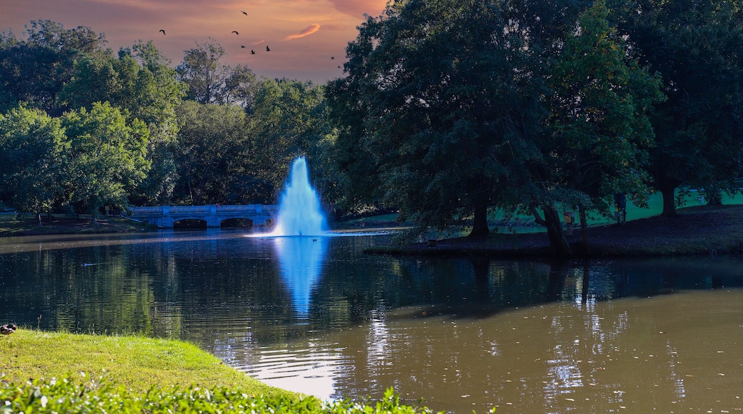 a gorgeous shot of the silky green lake water with a fountain in the middle of the lake with a stone bridge surrounded by lush green and autumn colored trees at Lenox Park in Brookhaven Georgia USA