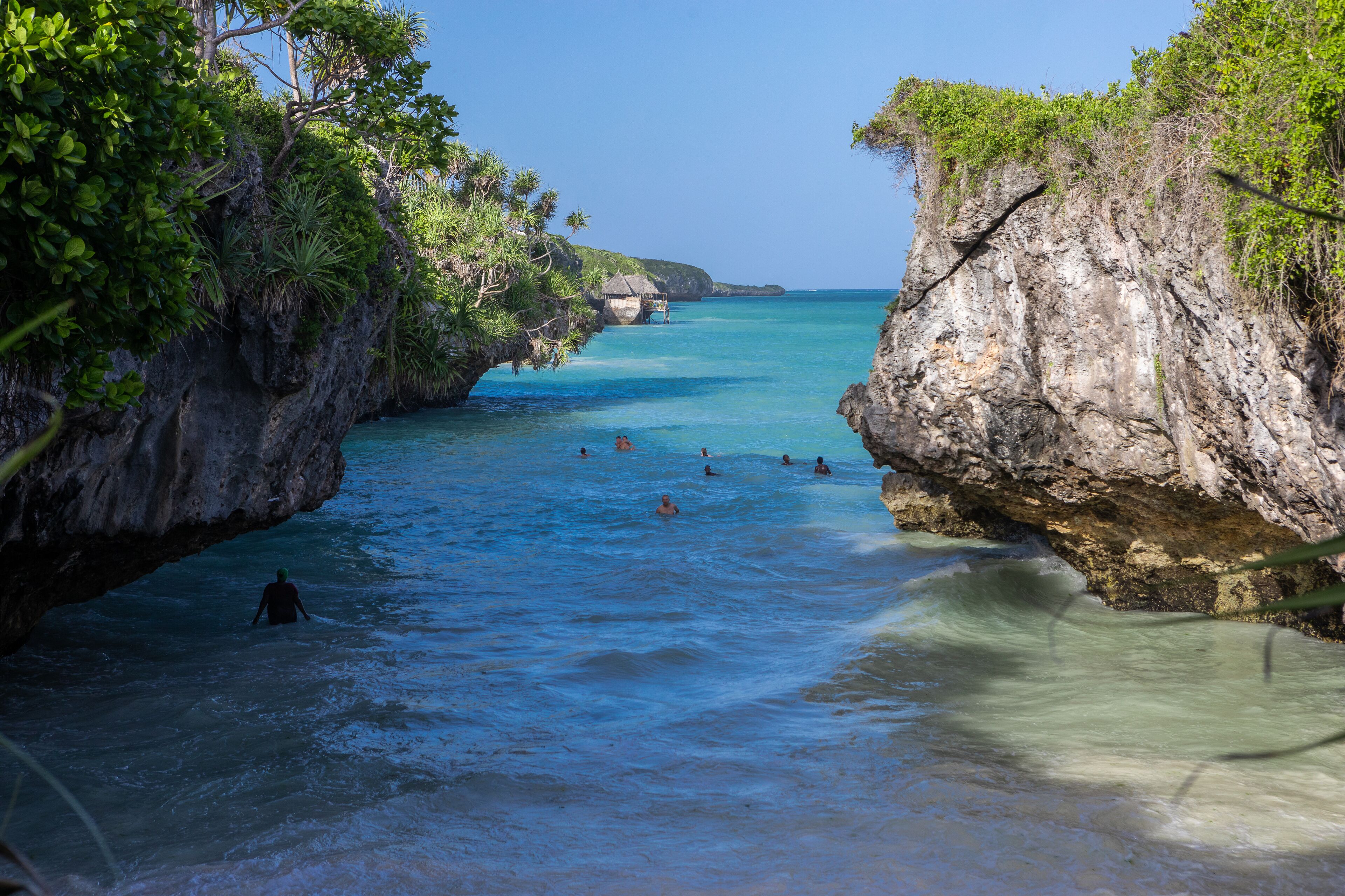 A coastal scene with clear turquoise water, rocky cliffs, and lush greenery.