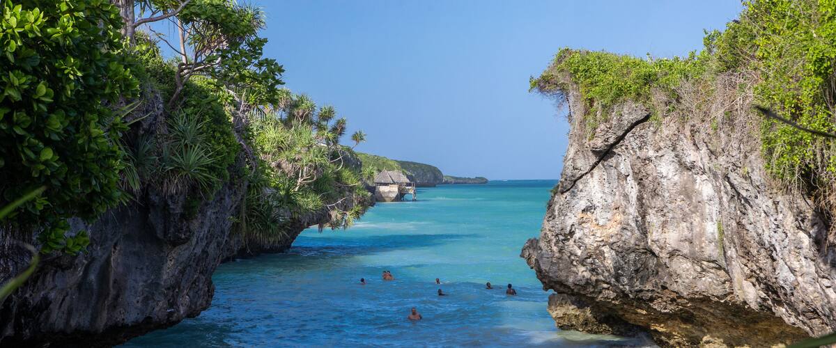 A coastal scene with clear turquoise water, rocky cliffs, and lush greenery.