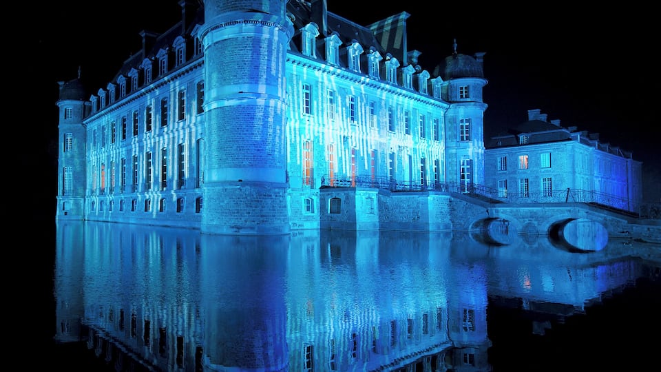 A large, illuminated castle with a prominent tower and a moat.