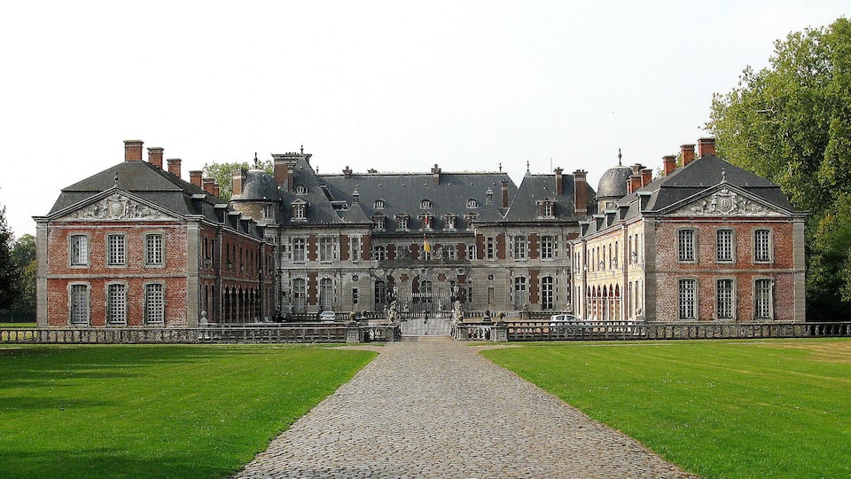 A large, historic building with a symmetrical facade, a central entrance, and a cobblestone pathway leading to it.