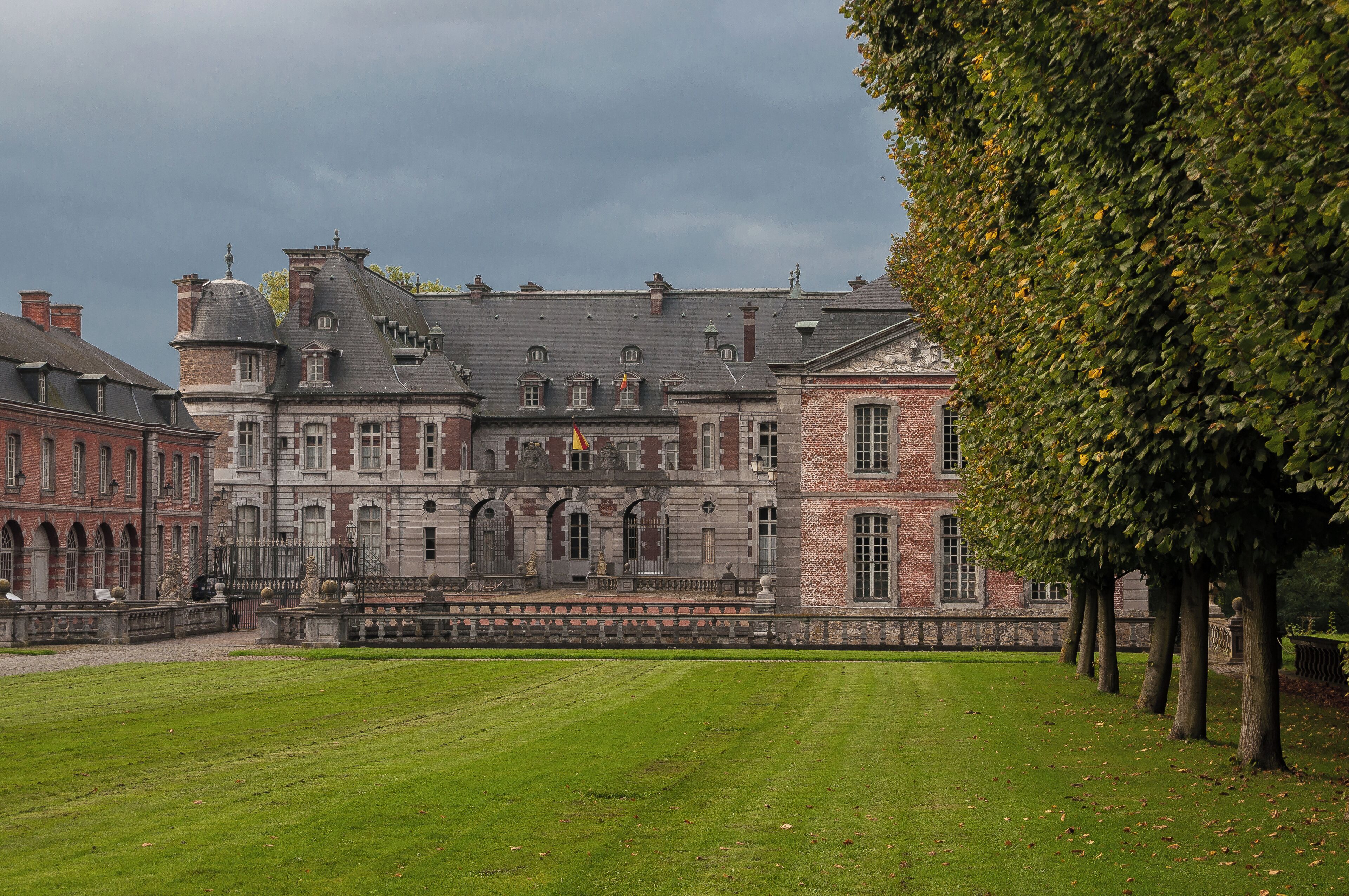 A historic building with a large lawn and trees in front.