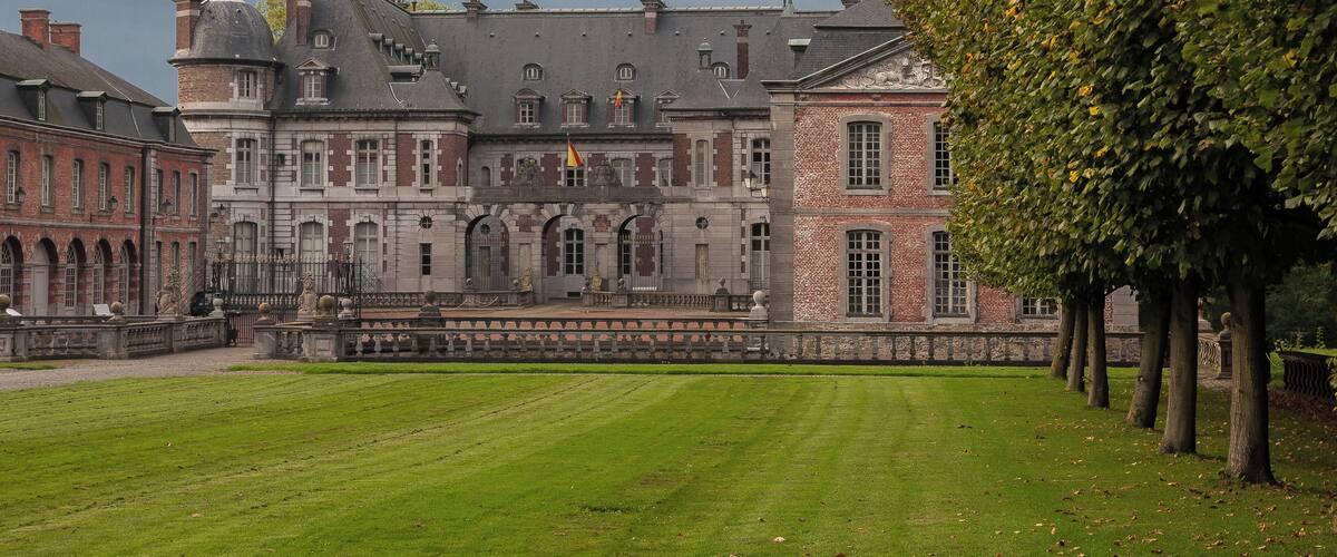 A historic building with a large lawn and trees in front.