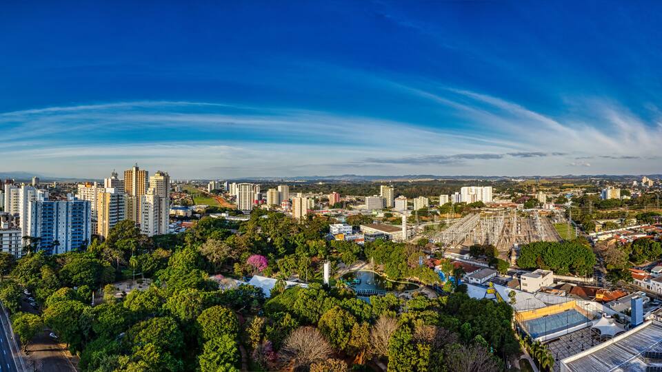 A cityscape with high-rise buildings, a stadium, and dense greenery.