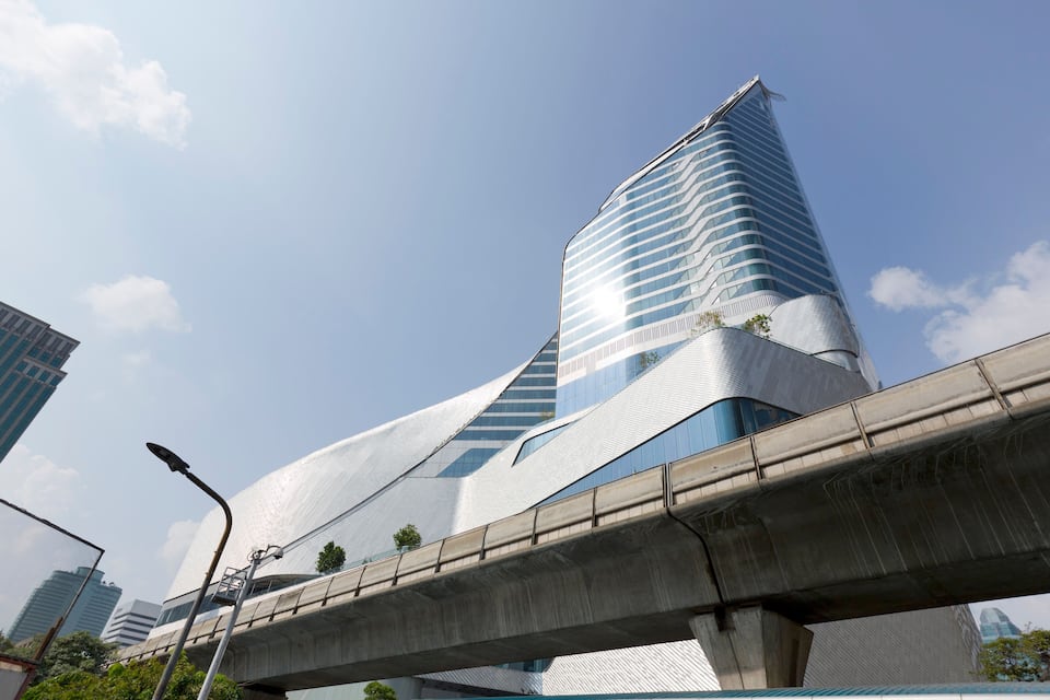 A modern skyscraper with a curved design, an elevated train track, and a clear blue sky.