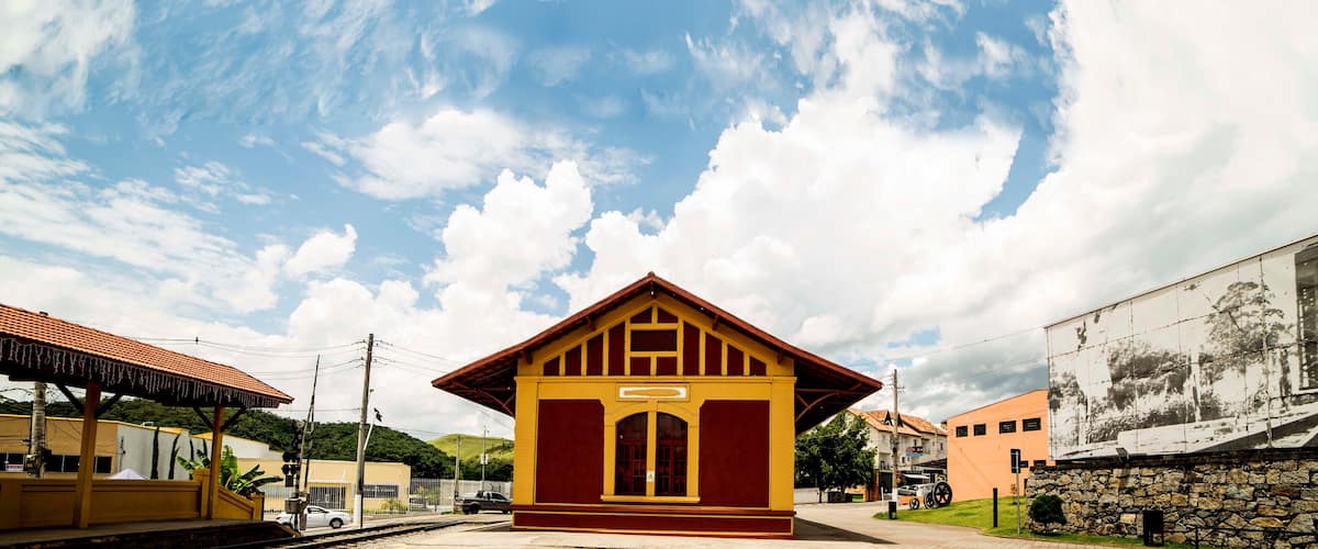 A small yellow train station with a red roof, surrounded by a stone wall and a mural.