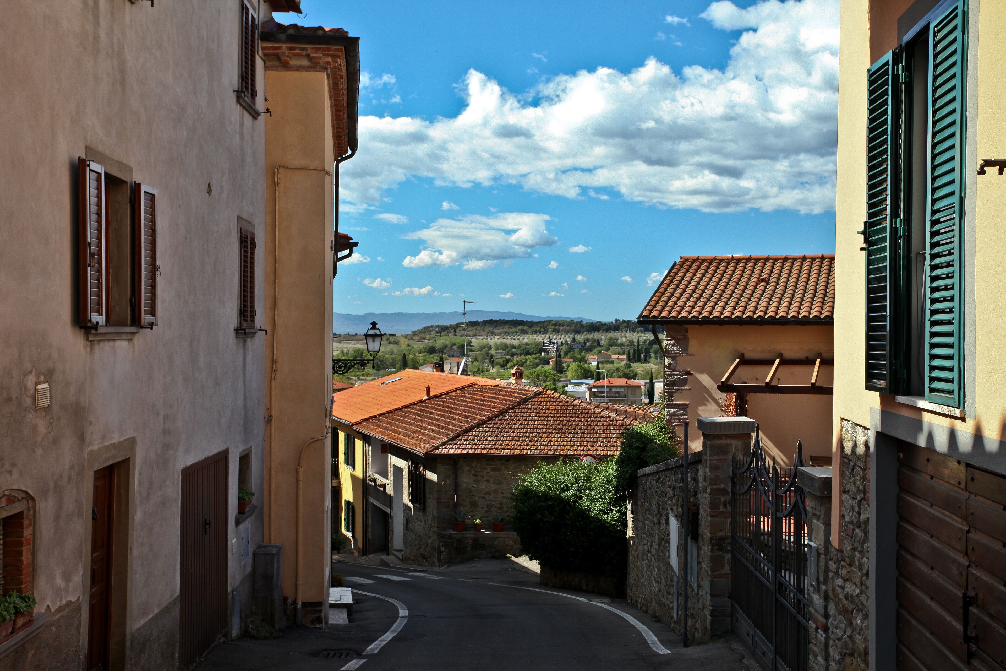 A narrow street in a historic town with terracotta-roofed buildings and a clear blue sky.