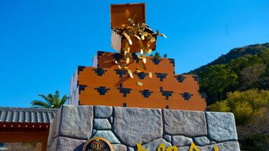 A pyramid-like structure with a golden statue on top, set against a clear blue sky and a mountainous backdrop.