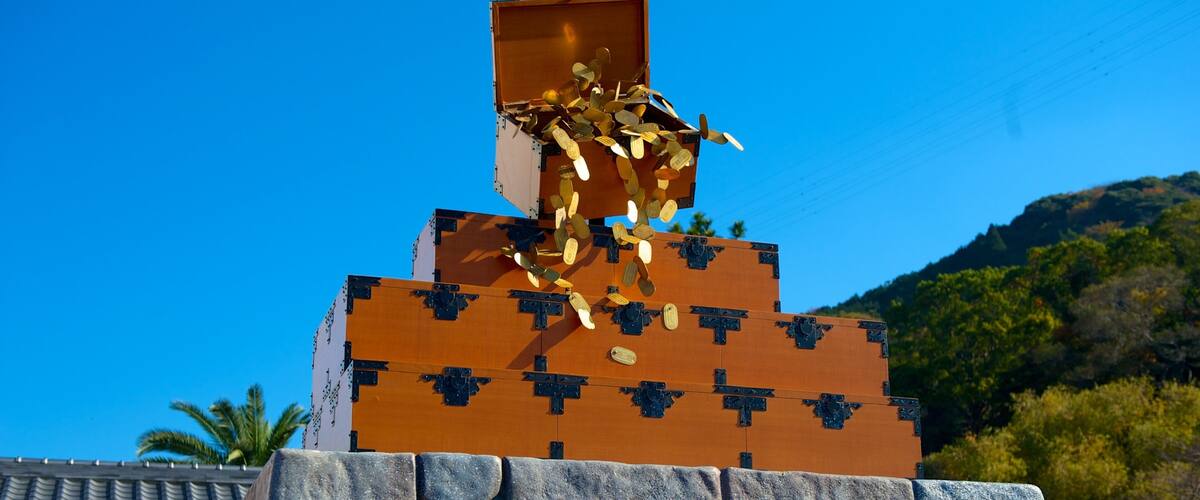 A pyramid-like structure with a golden statue on top, set against a clear blue sky and a mountainous backdrop.