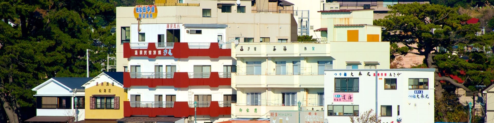 A coastal town with colorful buildings, a beach, and a forested hillside.