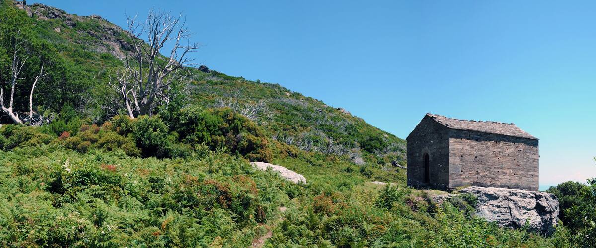 A stone building on a hillside with dense green vegetation and a clear blue sky.