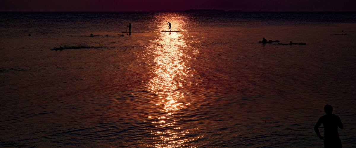 A sunset over a calm sea with a person standing on the shore.