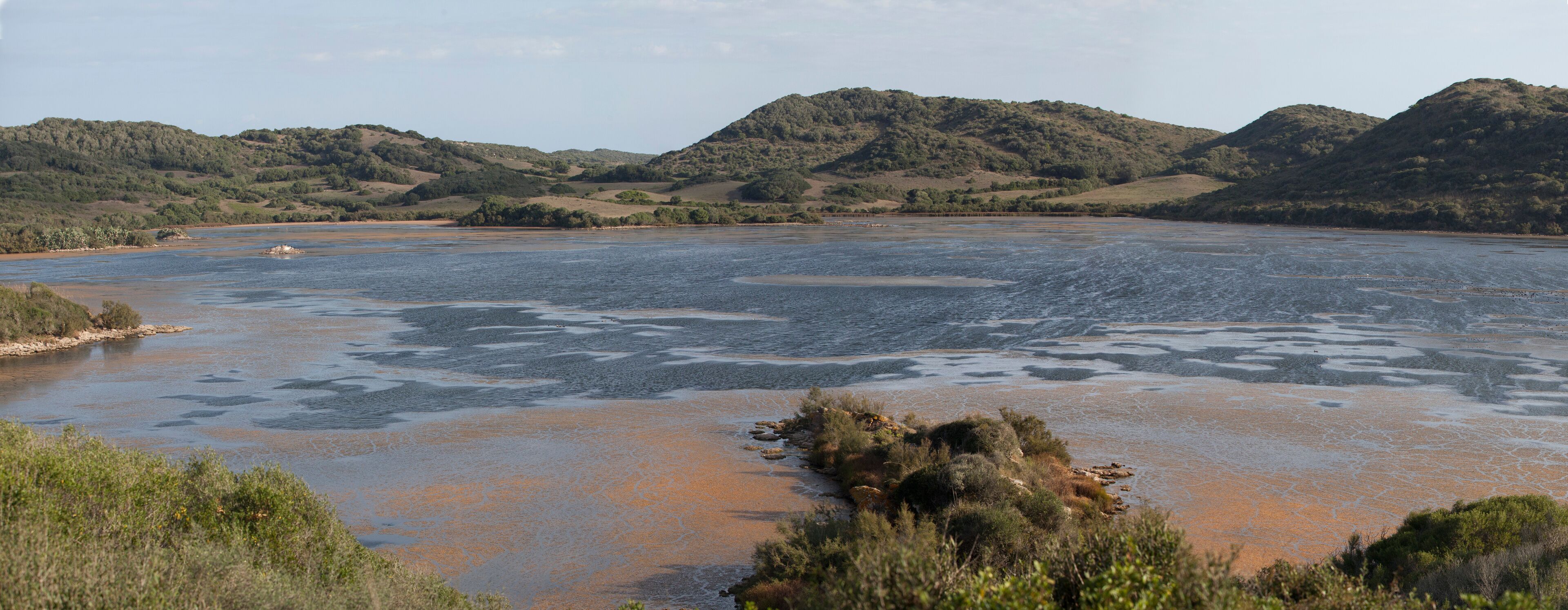 A river with surrounding hills and sparse vegetation.