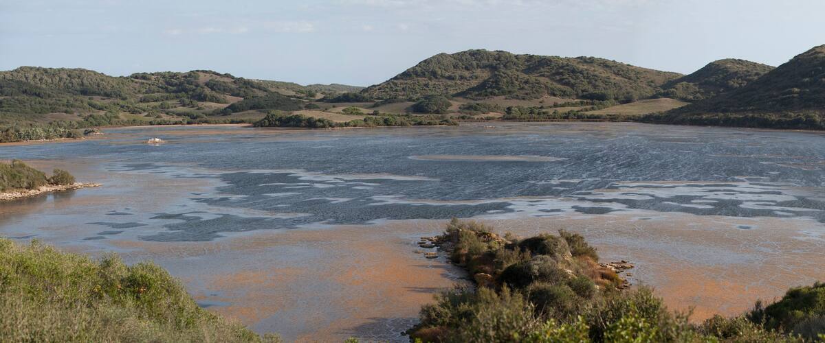 A river with surrounding hills and sparse vegetation.