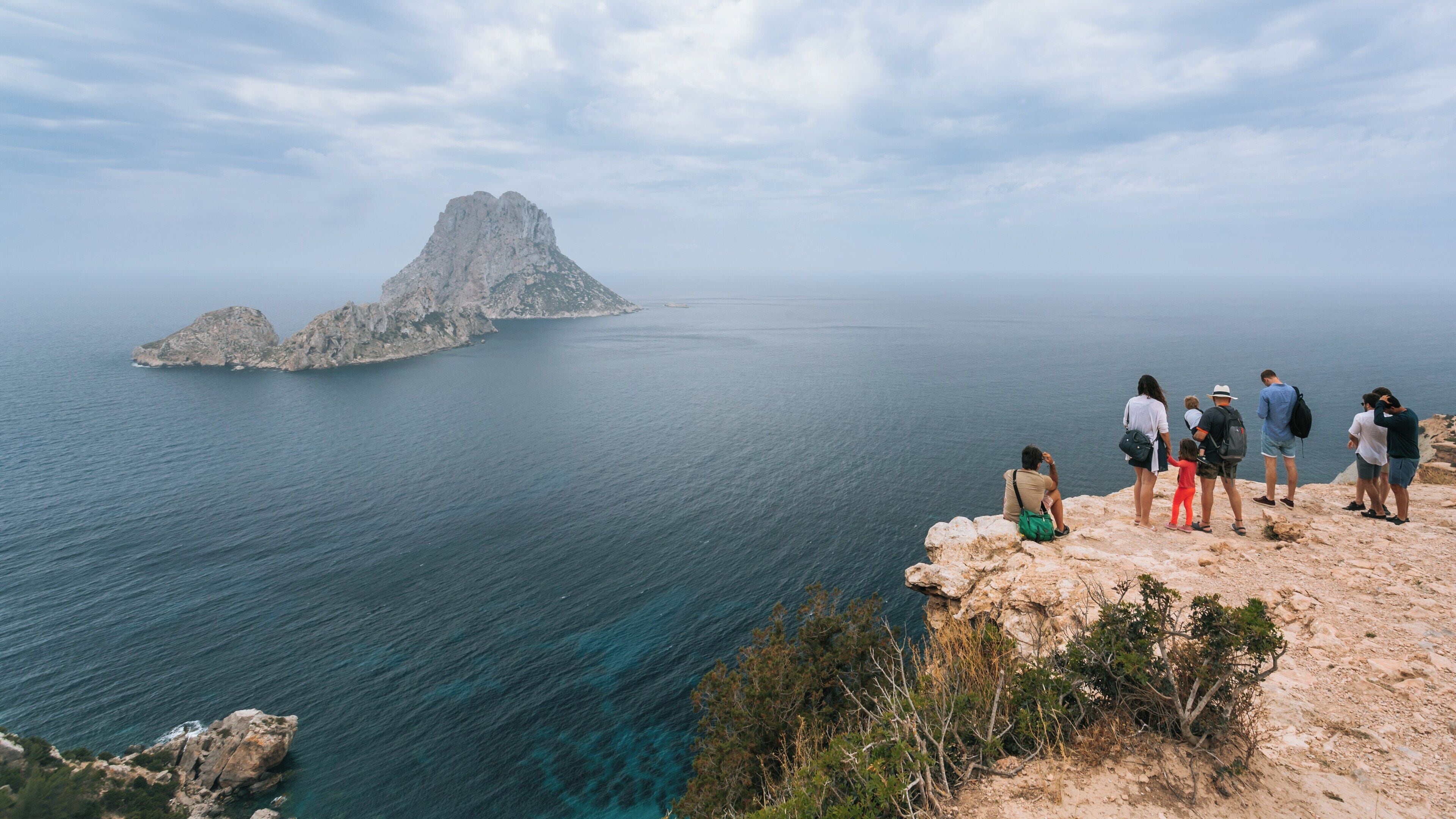 Visitors admire the stunning views of Es Vedrà, a striking island near Sant Josep de sa Talaia in the Balearic Islands of Spain on a cloudy day