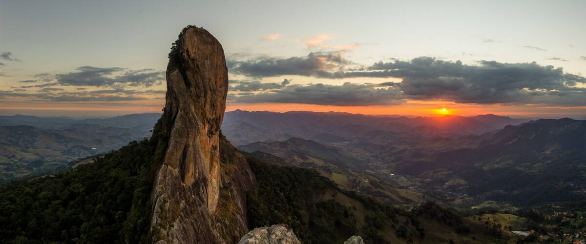 A mountain landscape with a prominent rock formation and a sunset in the background.