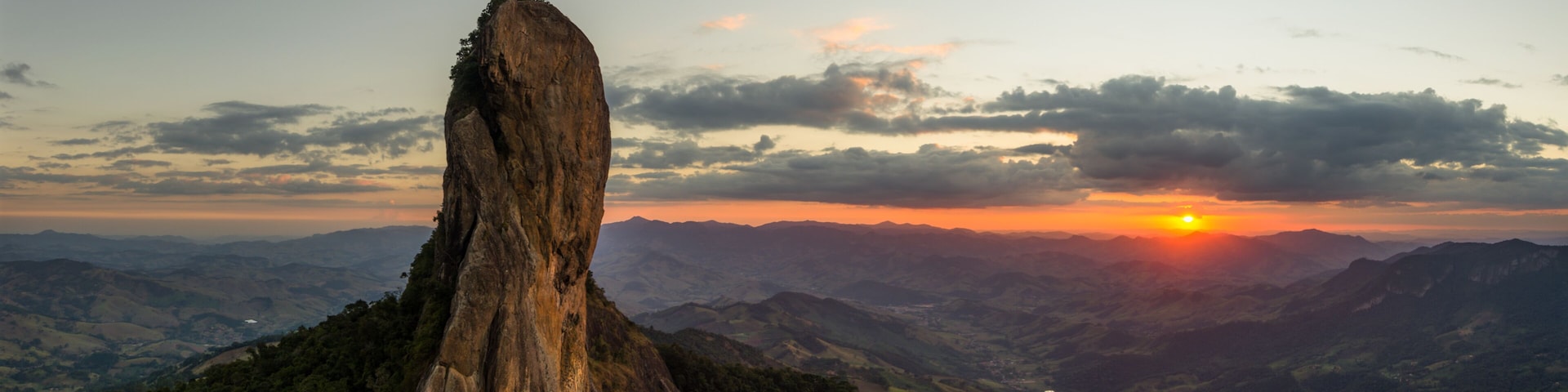 A mountain landscape with a prominent rock formation and a sunset in the background.