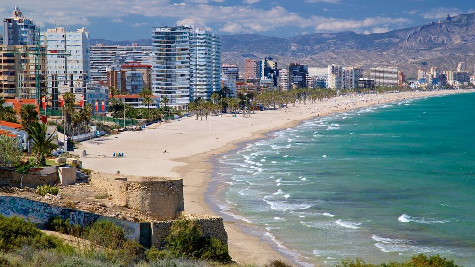 A coastal city with a sandy beach, a clear blue sea, and modern high-rise buildings.
