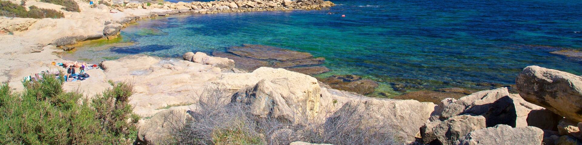 A rocky coastline with clear blue waters and a few people sunbathing.