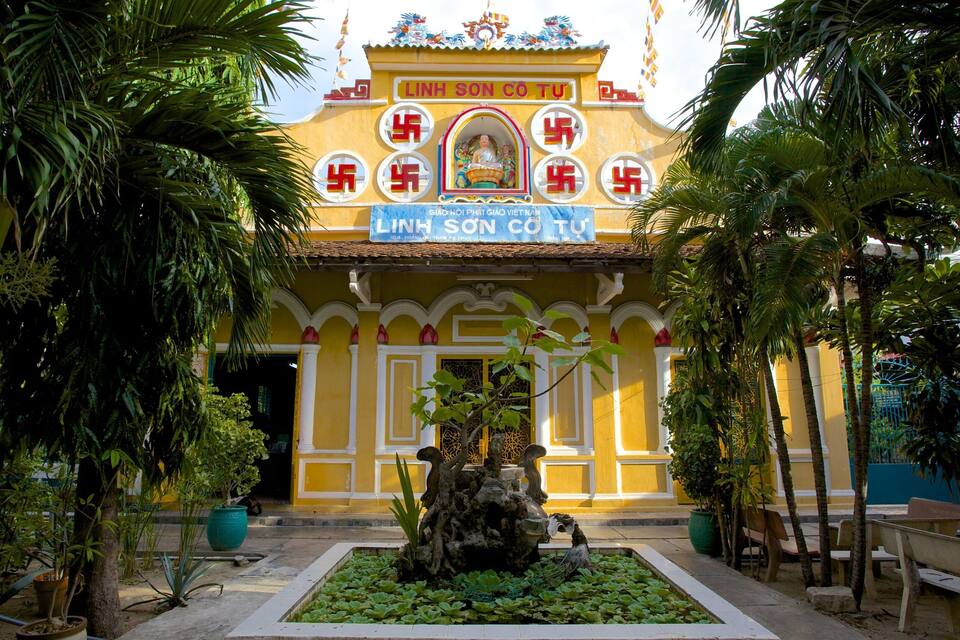 A temple with a statue in the center, surrounded by a pond and palm trees.