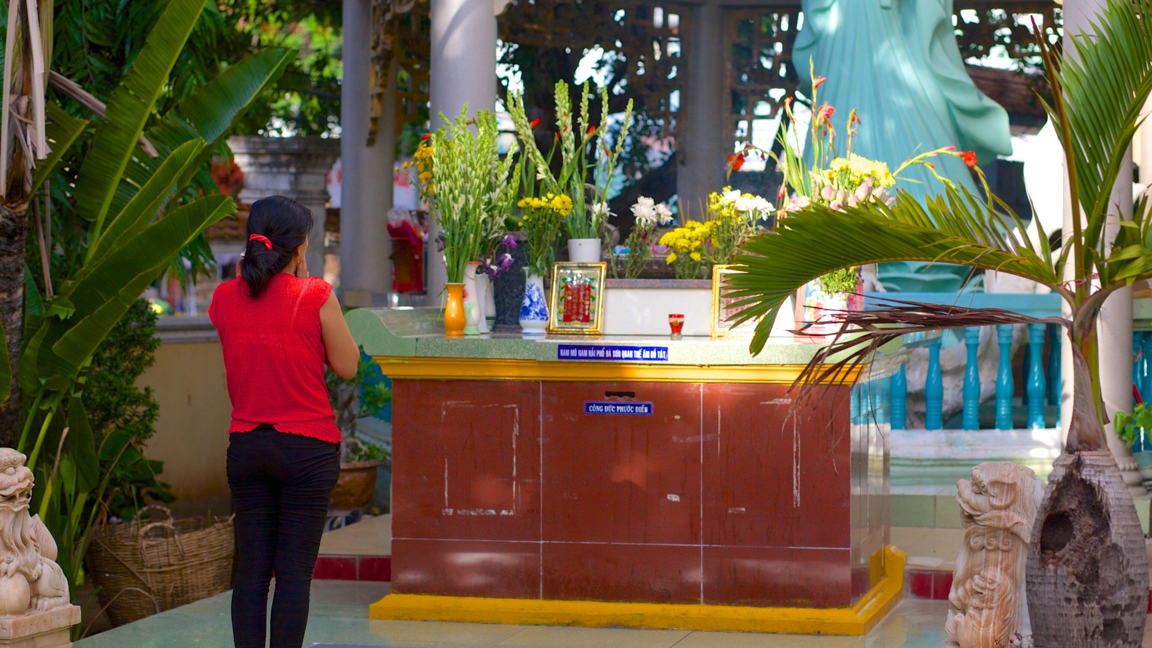 A woman praying at a temple altar with flowers and statues.