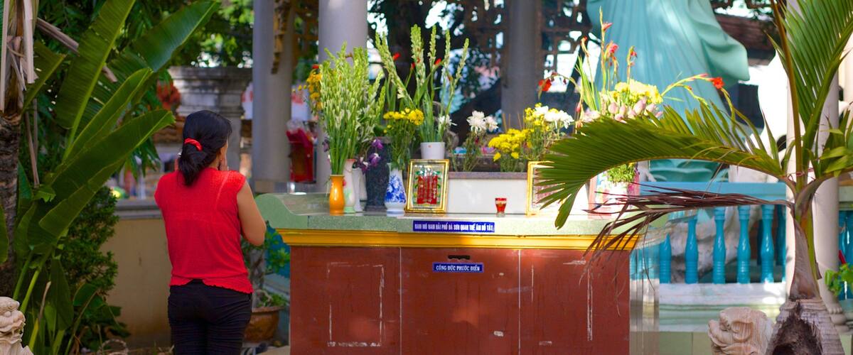 A woman praying at a temple altar with flowers and statues.