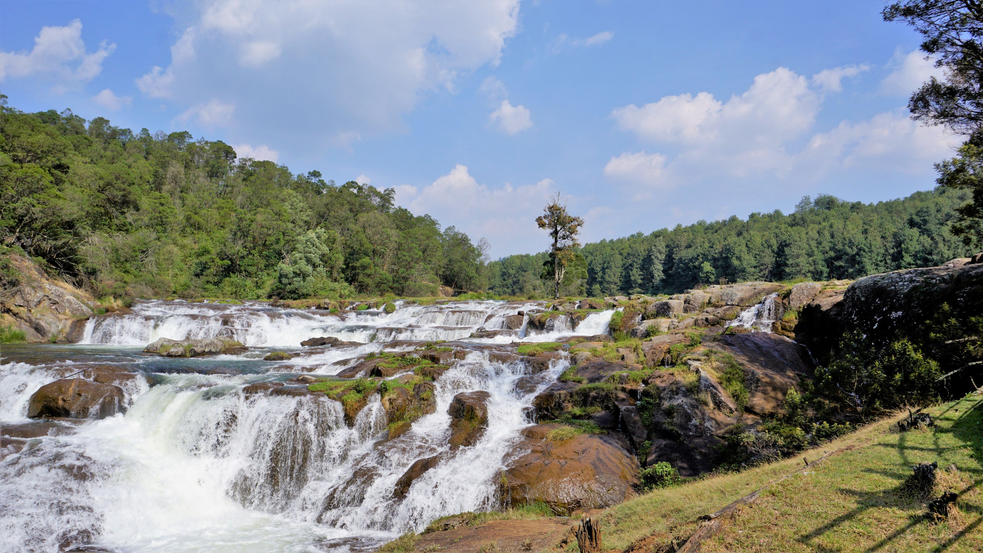 Ein mehrstufiger Wasserfall, umgeben von üppigem Grün und blauem Himmel.