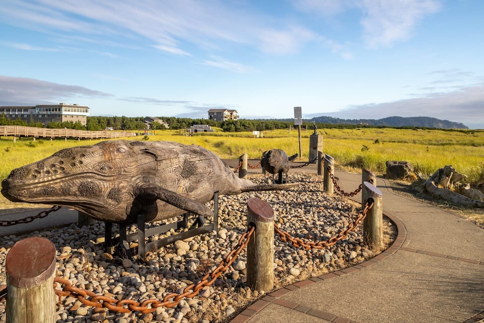 A large dinosaur sculpture in a park with a pathway, surrounded by rocks and chains.