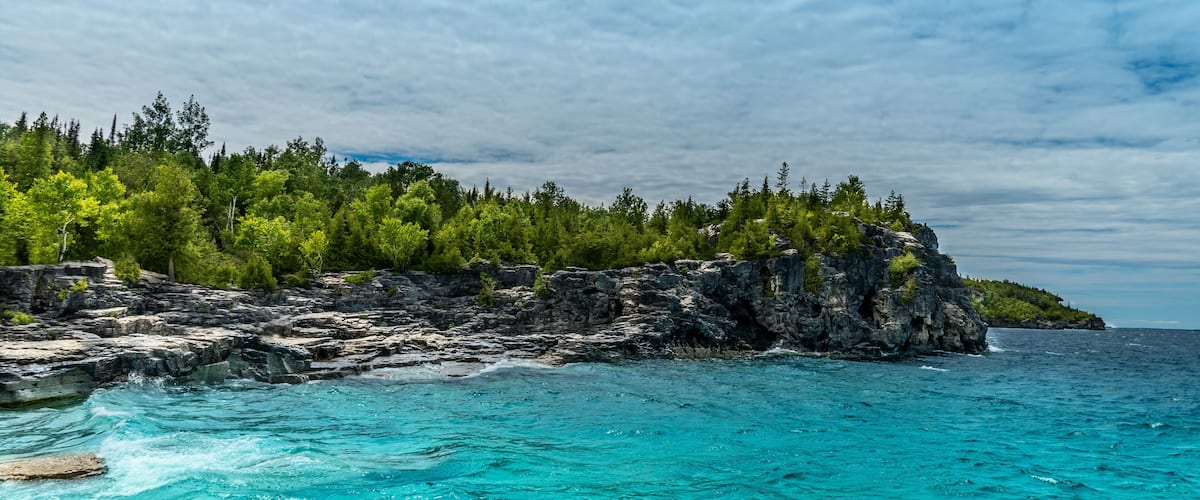 A rocky coastline with turquoise waters and a forested island.
