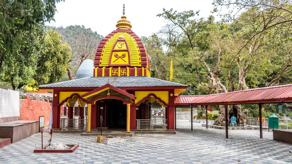 A temple with a yellow and red roof, surrounded by trees and a checkered pavement.