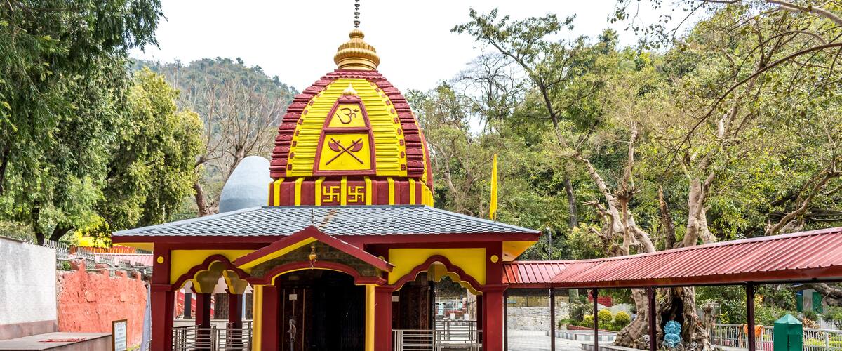A temple with a yellow and red roof, surrounded by trees and a checkered pavement.