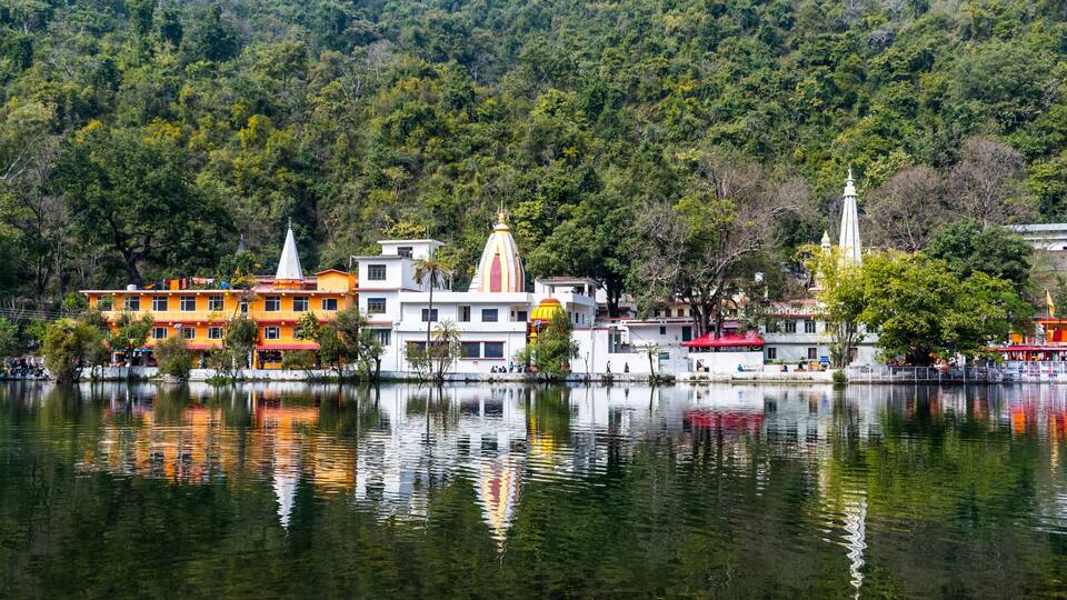 A lakeside town with colorful buildings, including a temple with a spire, surrounded by dense forest.