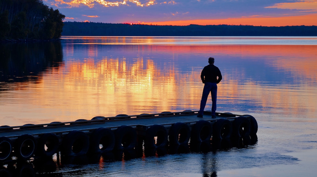 Silhouette Of A Person Standing At The End Of A Dock Looking Out Over A Tranquil Lake At Sunset, Gregoire Lake Provincial Park; Alberta, Canada
